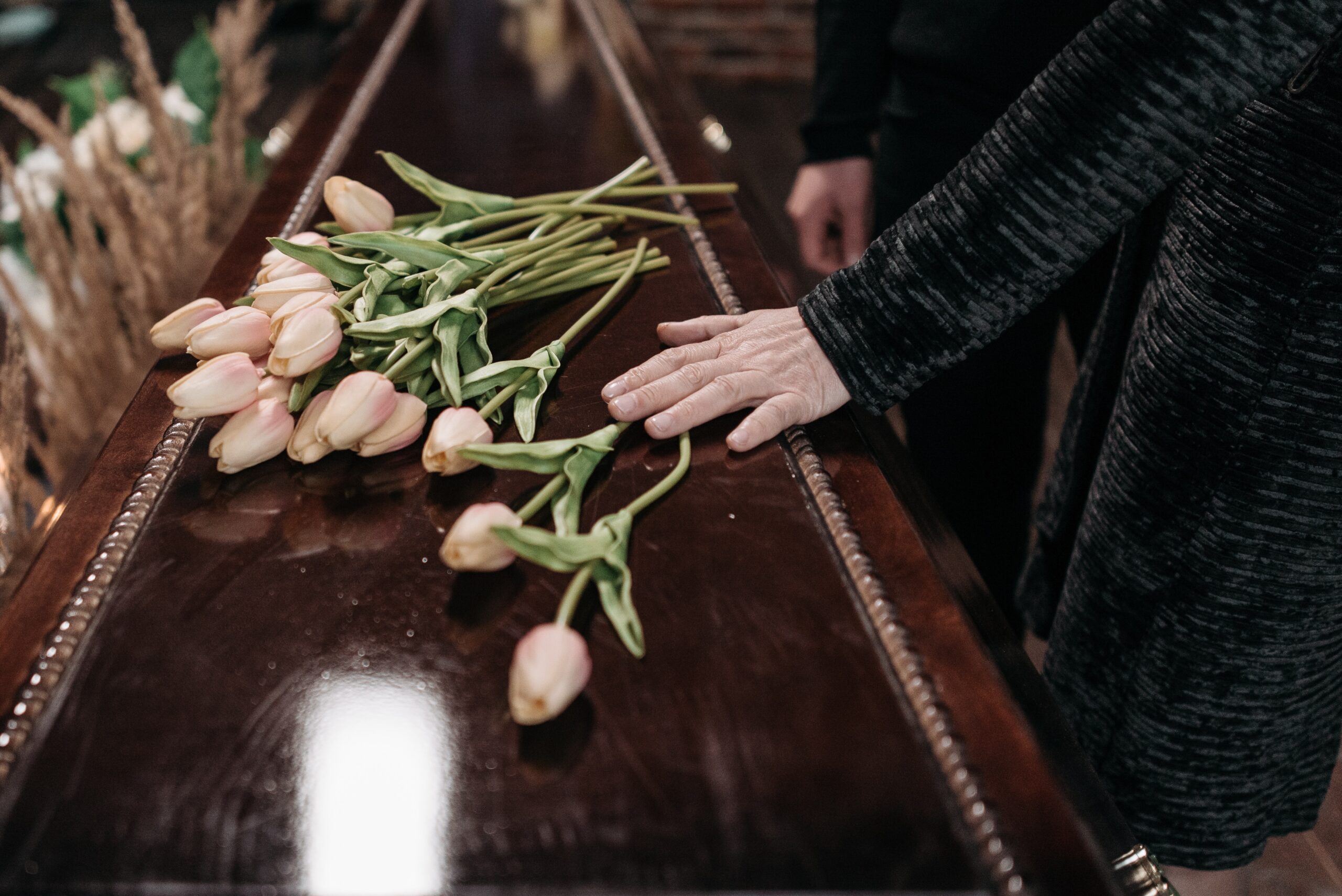 woman with hand on coffin covered in flowers
